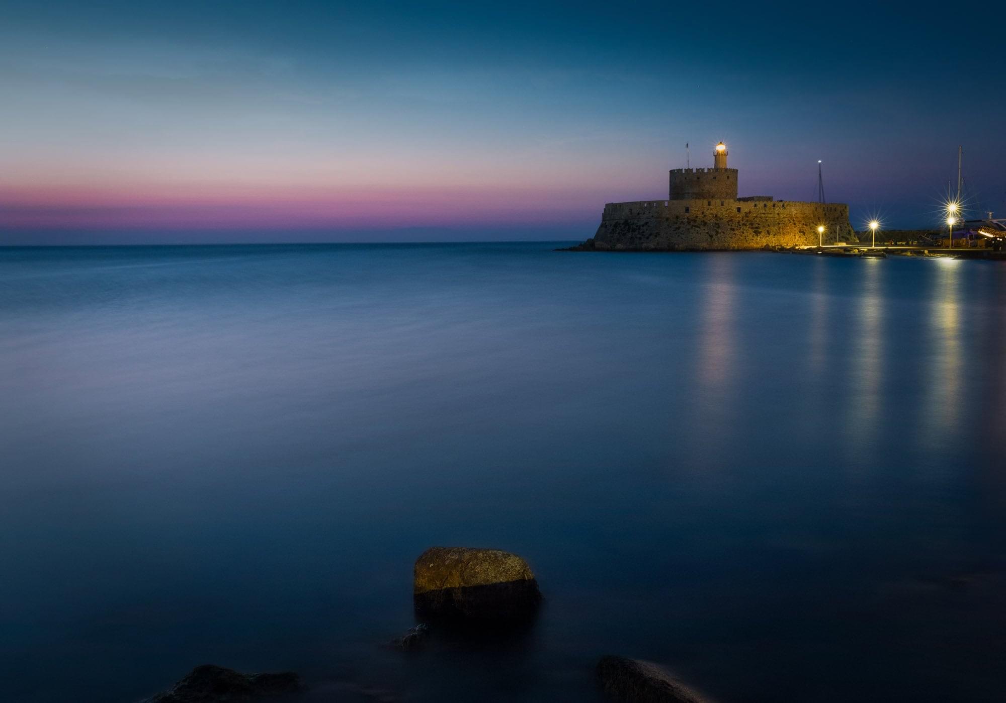 "The St. Nicholas Fortress at Mandraki Harbour, Rhodes, captured in the cool blue light of pre-dawn. Fine art photography available as a 100% cotton canvas or Limited Edition Giclée print, featuring a 1.5-inch (3.8 cm) solid Latvian pine frame."